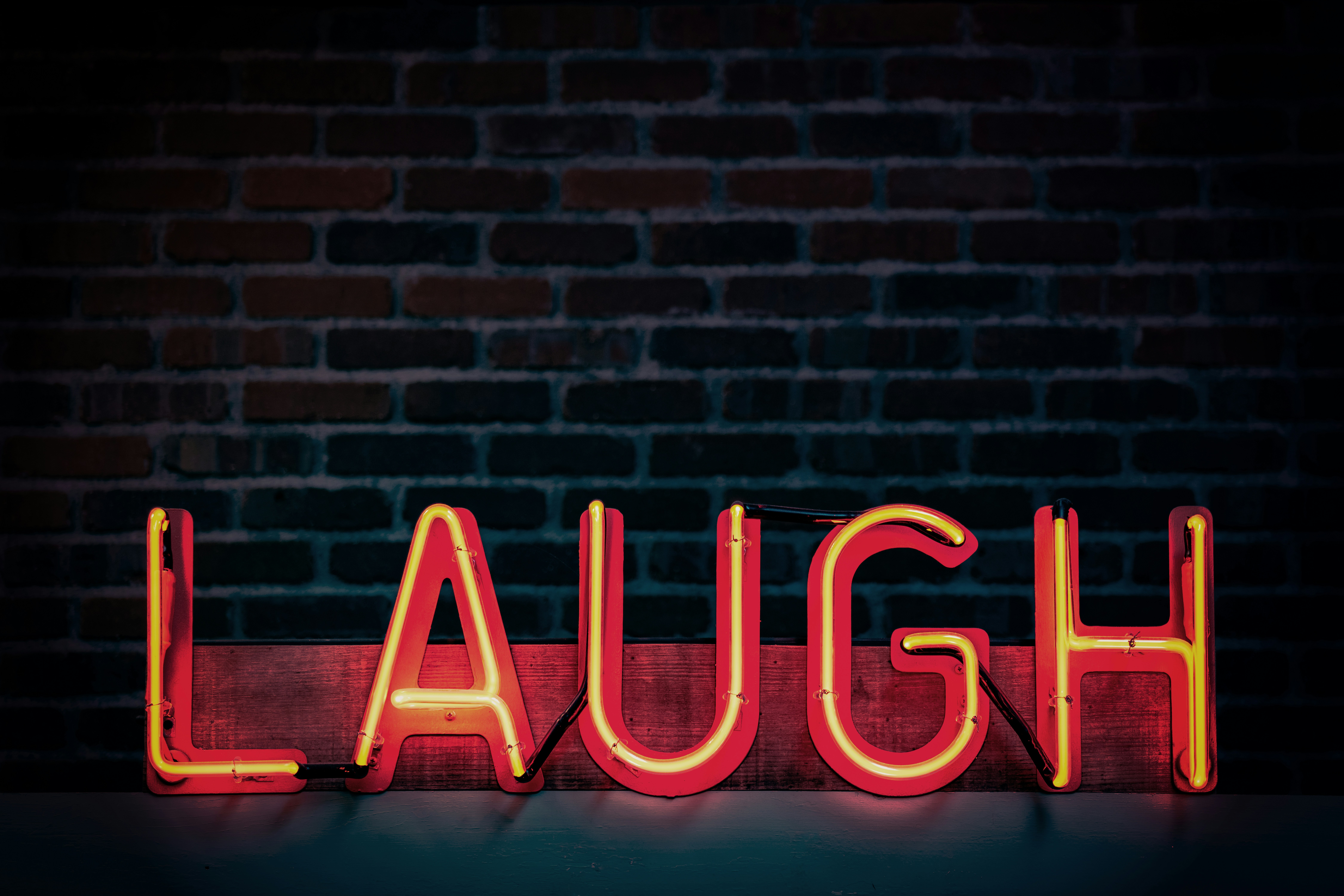 Neon sign spelling laugh against a dark brick wall